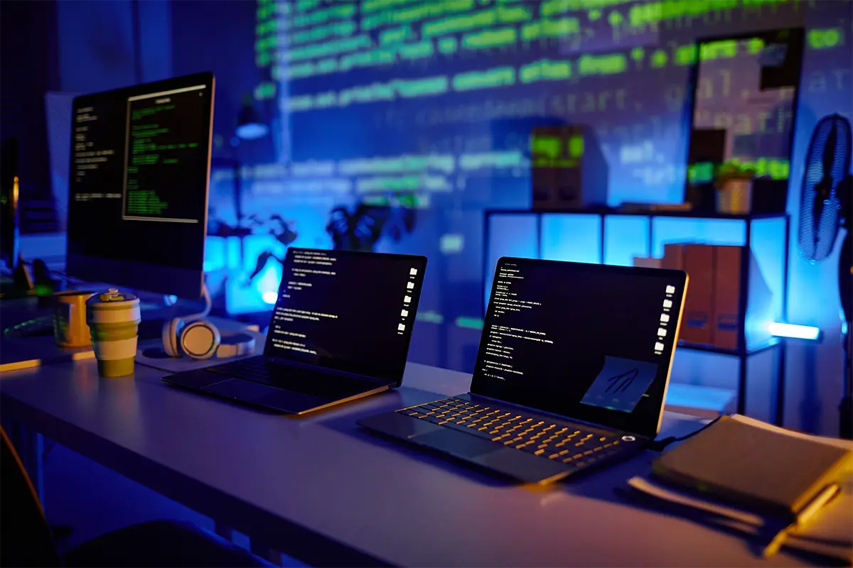 Desk with multiple computers on it all showing code
